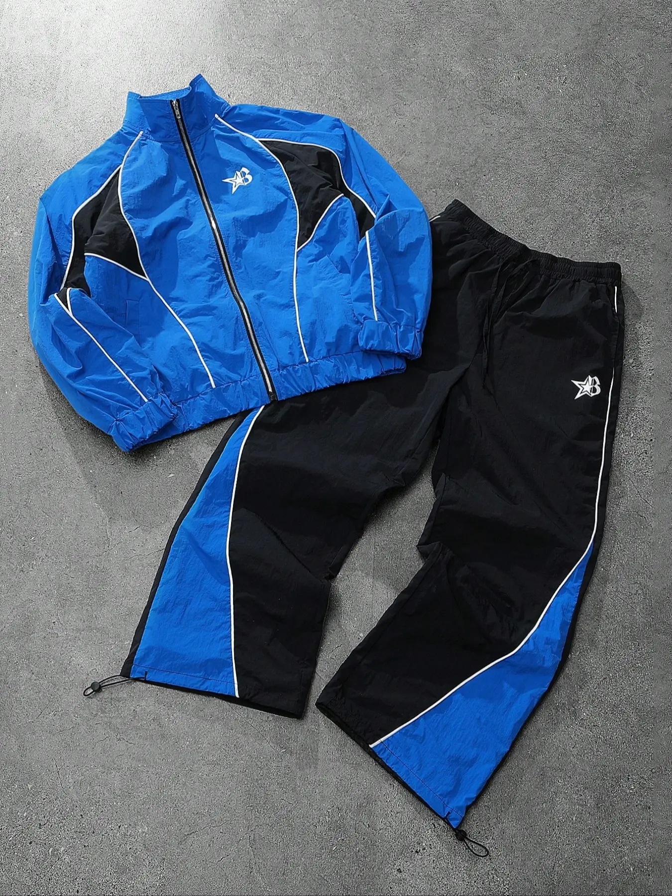 このメンズ2点セットのジャージは独特なツヤのあるブルー×ブラックのカラーブロックデザインが目を引くタートルネックジャケットとスウェットパンツで構成されています